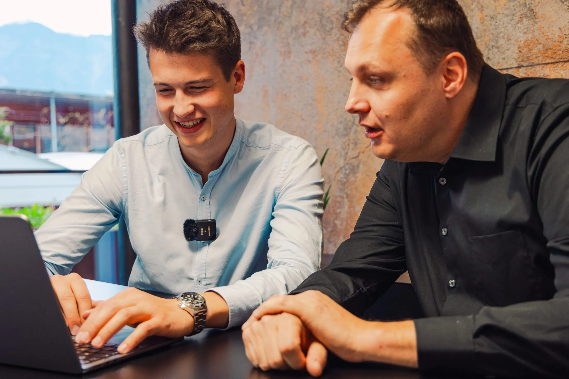 Zwei Kaino-Mitarbeiter lachen während der gemeinsamen Arbeit am Laptop